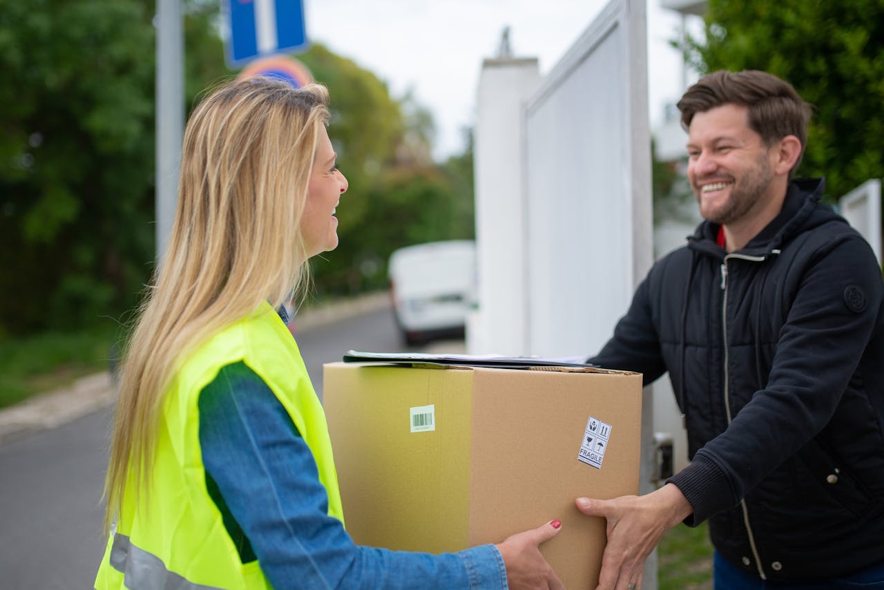 Smiling delivery woman hands over a package to a man outdoors in Portugal.